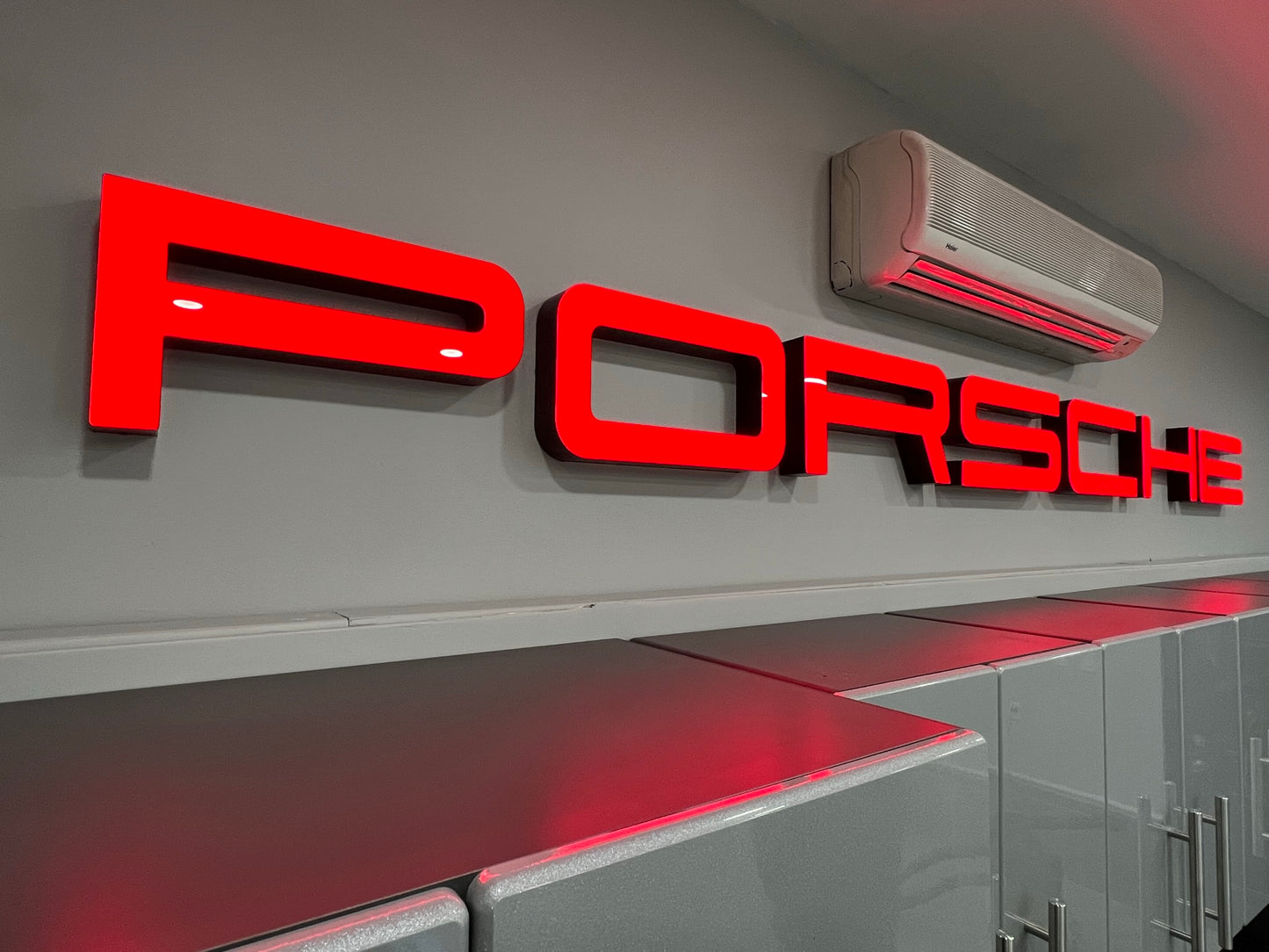 A red LED sign with the Porsche logo illuminated on a wall, presumably part of a dealership sign setup.